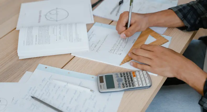 Student studying math with notes, calculator, and geometry tools on a desk while working on complex integrals