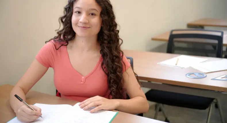 Student smiling in a classroom while writing notes in a notebook about complex integrals step by step